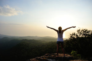 A woman standing on top of a mountain with her arms outstretched.